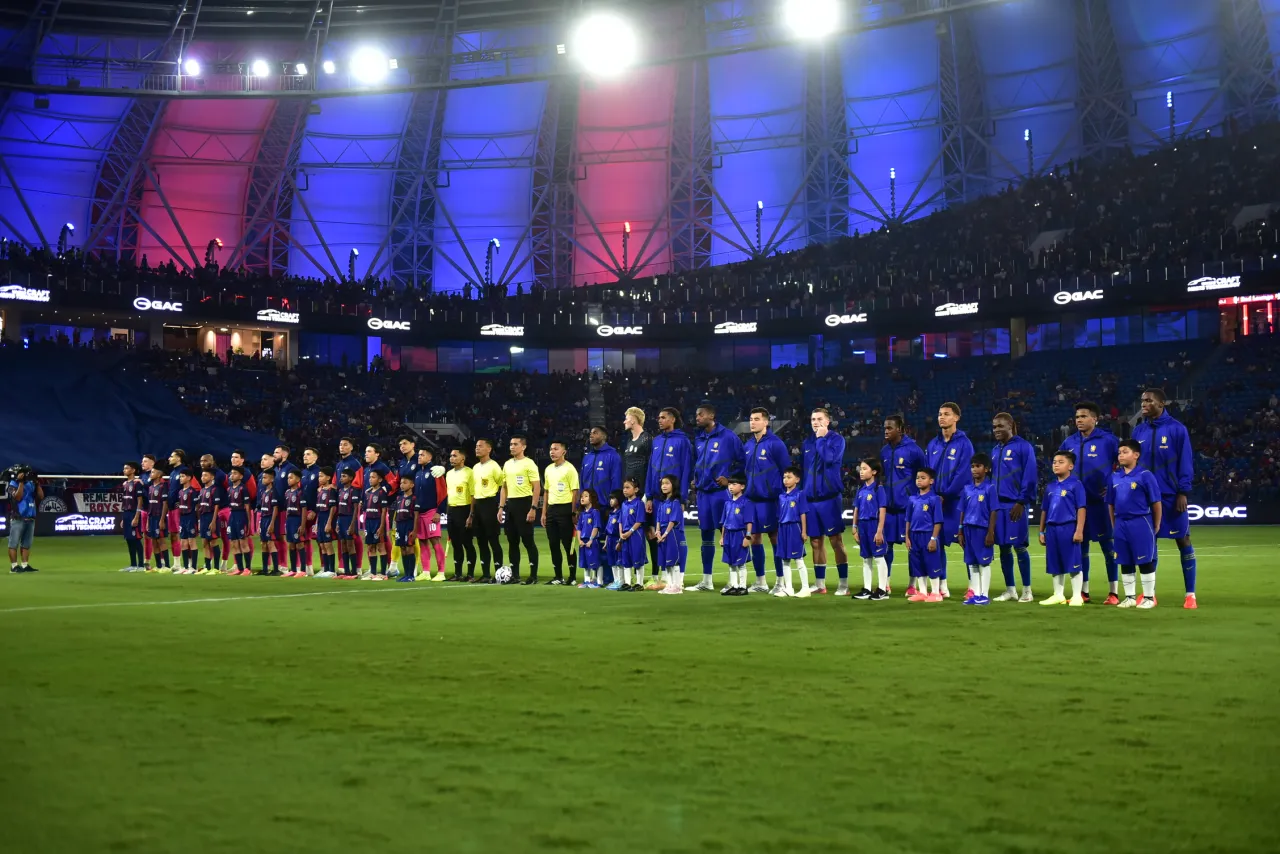 Johor Darul Ta'zim and Chelsea players line up with the match officials and player escorts before kick-off at Sultan Ibrahim Stadium.
